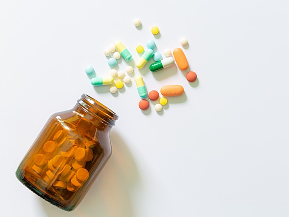 variety of pills spilling out of brown medication bottle